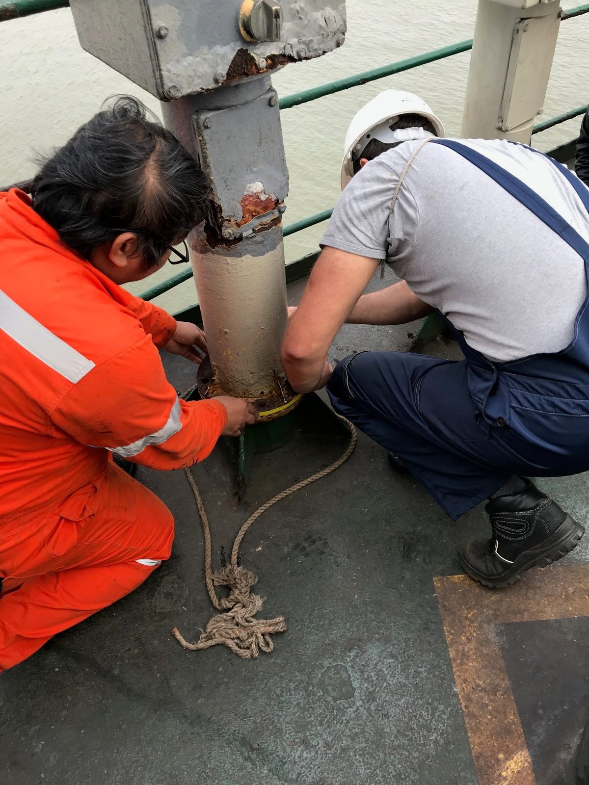Two technicians working at the base flange of deck equipment