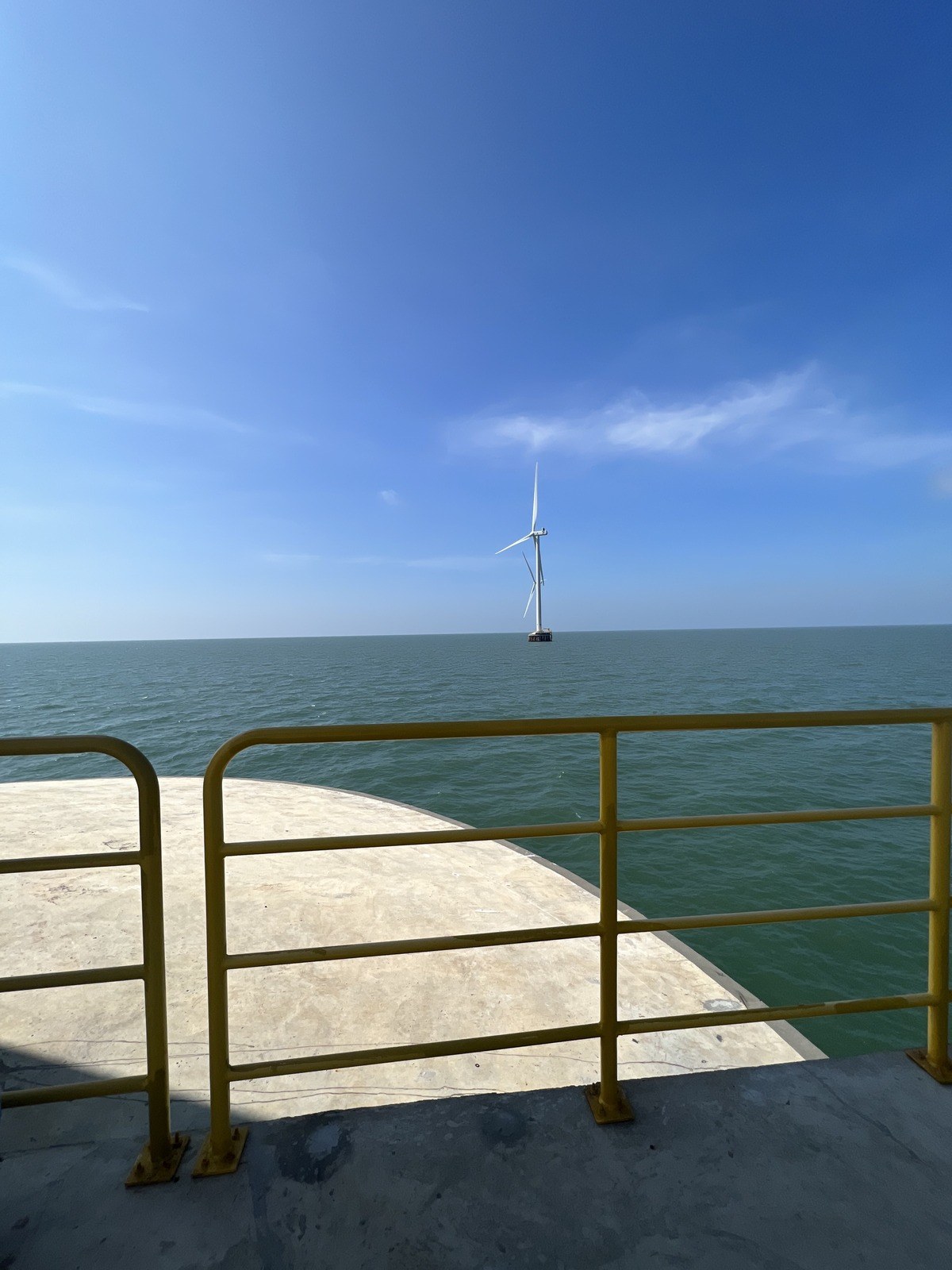 Offshore wind turbine seen from the railing of another foundation