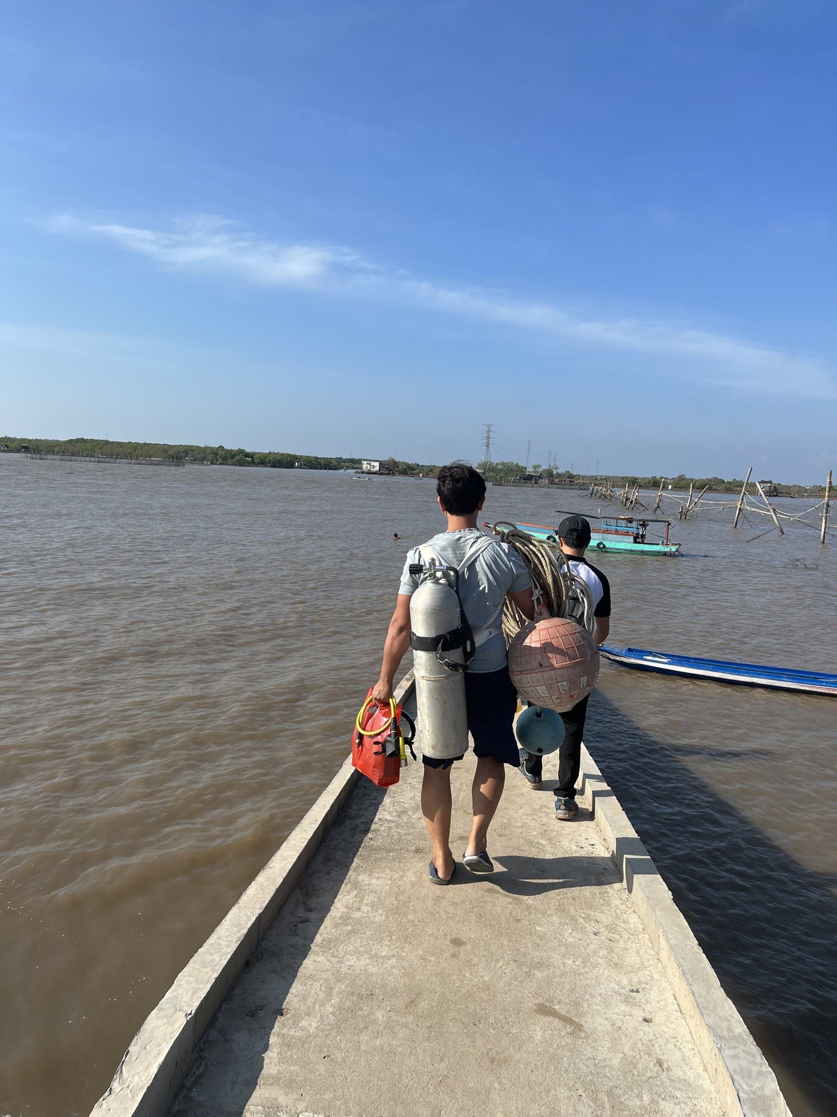 Divers carrying cylinders and marker buoys along a jetty to the work boat